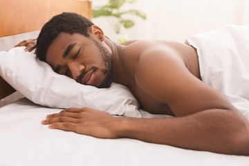 Naked black man sleeping in bed at home