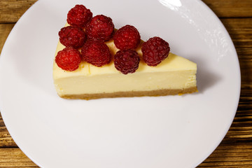 Piece of tasty New York cheesecake with raspberries in a white plate on wooden table