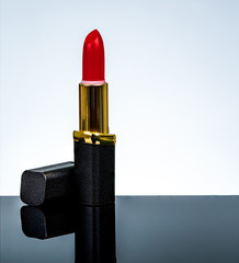 Red matte lipstick in gold and black tube package put on dark table isolated on white background in...