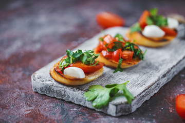 Italian bruschetta with tomatoes, mozzarella and herbs on a wooden board on a dark background