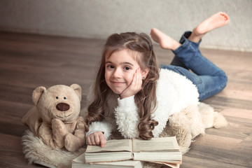 little girl reading a book with a Teddy bear on the floor, concept of relaxation and friendship