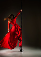 Slim woman in a sexy red dress and black stocking dancing on a pylon