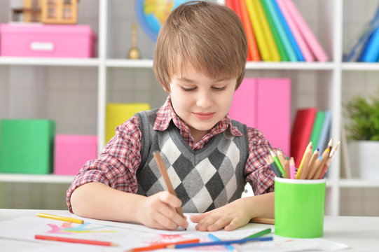 Portrait of little boy sitting at table and drawing with colorful pencils