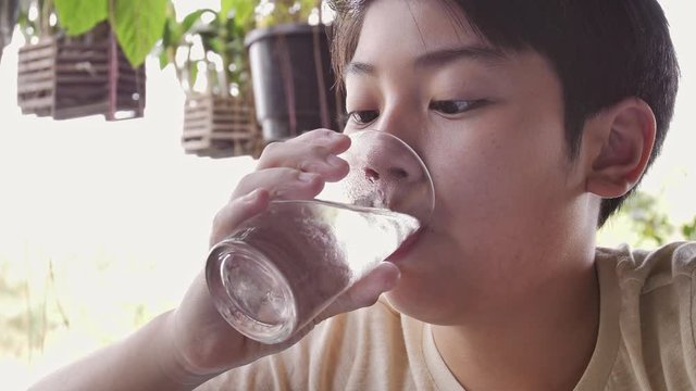 Slow motion of asian boy drinks water from a glass after breakfast, Close up teen boy with glass of water.