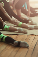 Shot of a row of young ladies doing gymnastic execrcises in a row. Girls raining together legs in a row no faces. Green elastic leg knee brace support for trainings