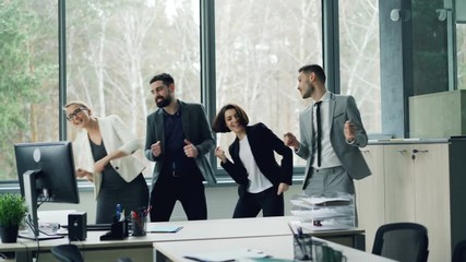 Group of happy carefree coworkers is dancing in office celebrating company event at party, laughing and having fun. Youth, job and emotions concept.