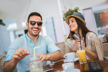 Happy young couple shopping online while sitting in a cafe. 