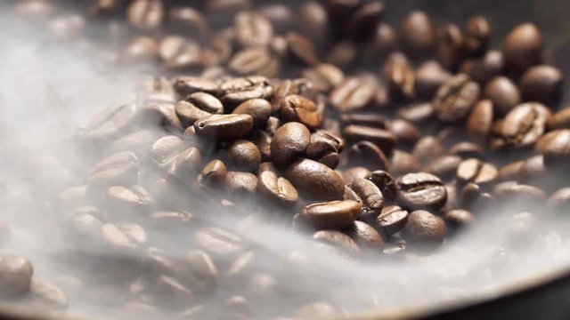 Fragrant coffee beans are roasted in a frying pan, smoke comes from coffee beans. The whole composition scrolls slowly around the camera. 