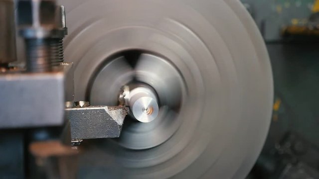 Chisel peeling spirals from a metallic rod fixed to a lathe cylinder on workshop  
