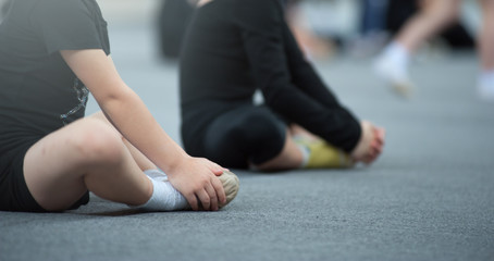 Young kids gymnast doing stretching exercises sitting on the floor dressed in black leggins. During...