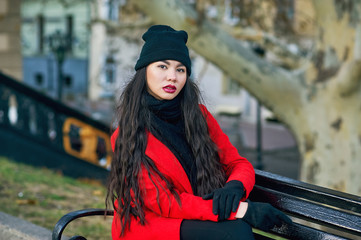 Portrait of a young beautiful fashionable woman in a red coat . Model posing on a city street