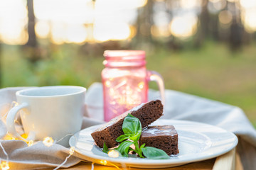 Coffee cup with a chocolate brownie cake decorated with mint on a table outdoor