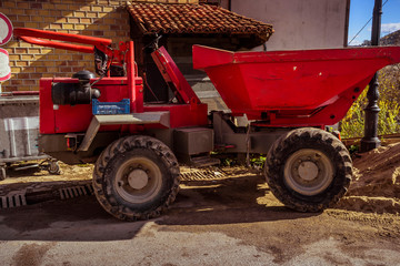 A big red dump truck in front of a building under construction.