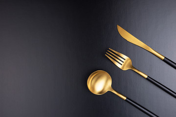 Set of black and gold cutlery on black background