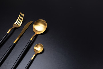 Set of black and gold cutlery on black background