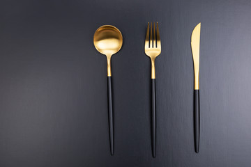 Set of black and gold cutlery on black background