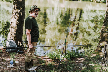 Full length of a pleasant aged angler holding nets while standing on the river bank