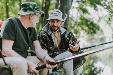 Pleasant man talking with his son while fishing