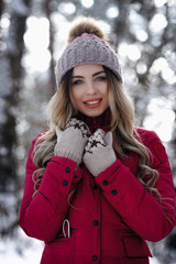 A beautiful woman in purple down jacket and kniited hat and gloves smile in winter snowly forest....
