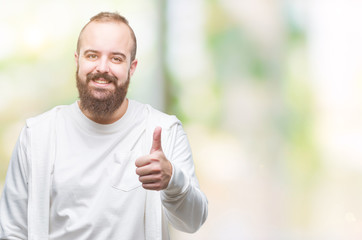 Young caucasian hipster man wearing sport clothes over isolated background doing happy thumbs up gesture with hand. Approving expression looking at the camera with showing success.