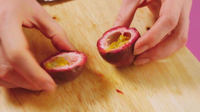top view, female hand cuts fruit with a knife on a wooden board, maracuya. The concept of natural healthy food.