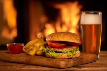 Hamburger with potato and beer on the fireplace background.