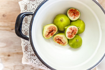 Cut ripe figs and antique knife in a vintage white enamel pot on an antique lace kitchen cloth and table