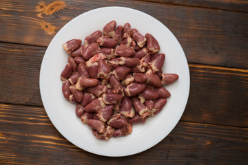 Raw chicken hearts on a white plate on a wooden background.