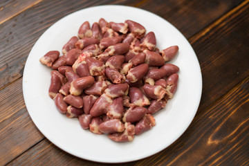 Raw chicken hearts on a white plate on a wooden background.