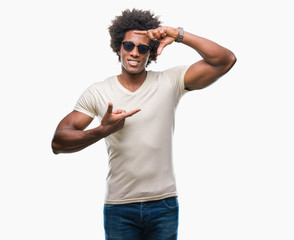Fototapeta premium Afro american man wearing sunglasses over isolated background smiling making frame with hands and fingers with happy face. Creativity and photography concept.