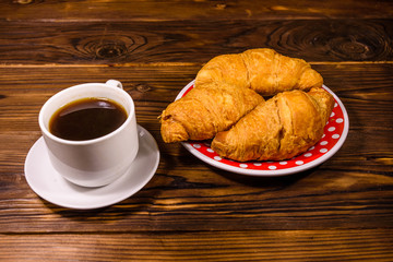 Cup of dark coffee and croissants on wooden table