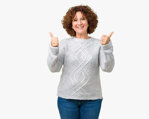 Beautiful middle ager senior woman wearing winter sweater over isolated background success sign doing positive gesture with hand, thumbs up smiling and happy. Looking at the camera