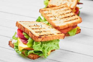 Three sandwiches with ham, lettuce and fresh vegetables on a white background