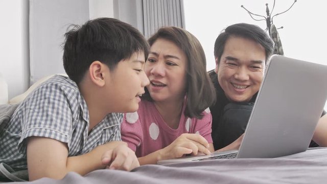 Happy family Father mother and son watching on laptop computer and having fun, Slow motion 4K  asian family rest on bed with laptop computer