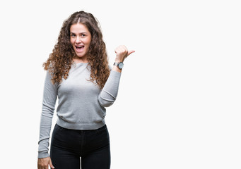 Beautiful brunette curly hair young girl wearing a sweater over isolated background smiling with happy face looking and pointing to the side with thumb up.
