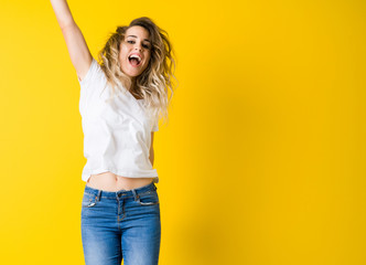Beautiful young blonde woman jumping happy and excited over isolated yellow background