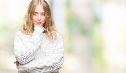 Obraz premium Beautiful young blonde woman wearing winter sweater over isolated background looking confident at the camera with smile with crossed arms and hand raised on chin. Thinking positive.