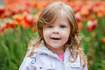 Cute curly hair blonde girl smiling with surprise on tulip bloss