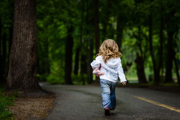 Little blonde girl walks away to dark park alone