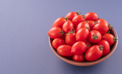 Fresh red cherry tomatoes in a wooden bowl isolated on a blue background, close up, copy space