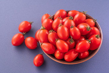 Fresh red cherry tomatoes in a wooden bowl isolated on a blue background, close up, copy space
