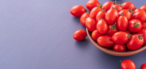 Fresh red cherry tomatoes in a wooden bowl isolated on a blue background, close up, copy space