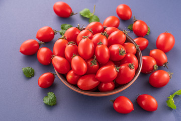 Fresh red cherry tomatoes in a wooden bowl isolated on a blue background, close up, copy space