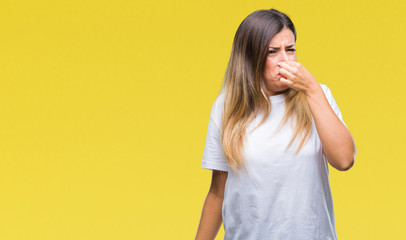 Young beautiful woman casual white t-shirt over isolated background smelling something stinky and disgusting, intolerable smell, holding breath with fingers on nose. Bad smells concept.