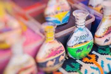 Fototapeta na wymiar Souvenirs from Jordan - bottles with sand and shapes of desert and camels. Selective Focus.