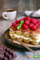 Homemade tiramisu with raspberry on a black plate.