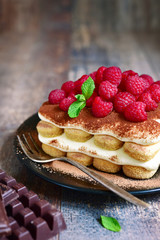 Homemade tiramisu with raspberry on a black plate.