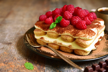 Homemade tiramisu with raspberry on a black plate.
