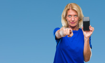 Middle age blonde woman showing blank screen of smartphone over isolated background pointing with finger to the camera and to you, hand sign, positive and confident gesture from the front