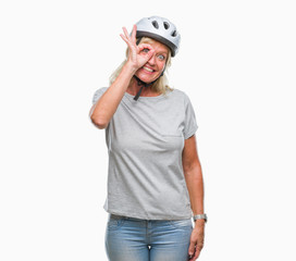 Middle age caucasian cyclist woman wearing safety helmet over isolated background doing ok gesture with hand smiling, eye looking through fingers with happy face.
